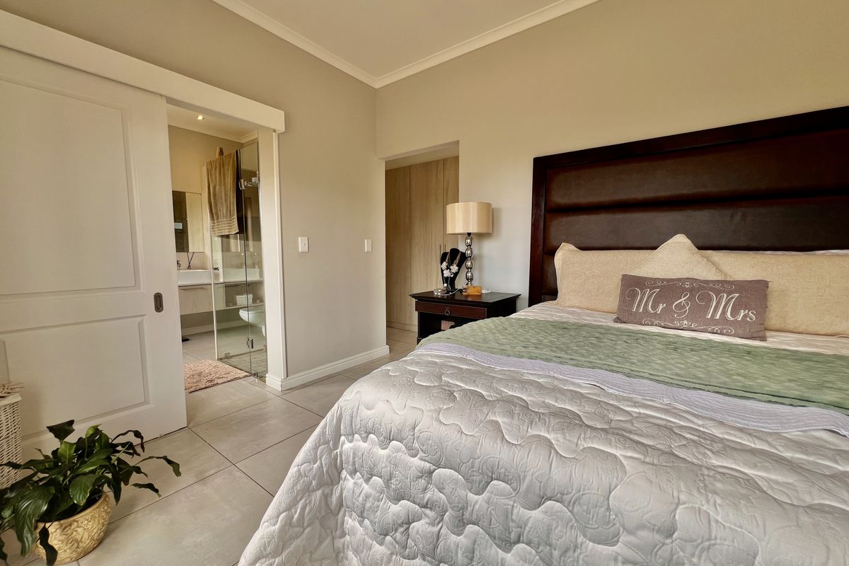 Spacious bedroom featuring neutral tiled flooring, built-in cupboards, and an en-suite bathroom accessed via a sliding door.