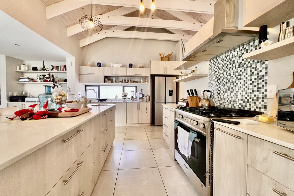 Modern open-plan kitchen featuring a large central island, gas range with extractor hood, mosaic tile backsplash, and vaulted timber-beamed ceilings.