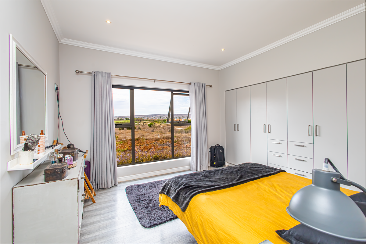 A bright bedroom featuring built-in floor-to-ceiling wardrobes, modern laminate flooring, and a large window offering scenic landscape views.