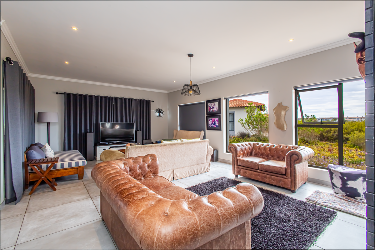 Spacious living room featuring large windows, tiled flooring, and recessed ceiling lighting, offering a bright and comfortable atmosphere with views of the garden.
