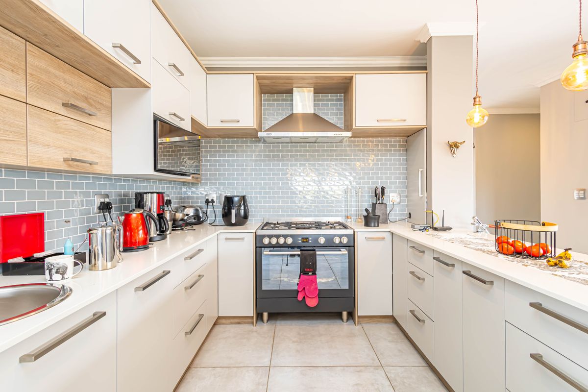 Modern U-shaped kitchen featuring light-toned cabinetry, subway tile backsplash, stainless steel extractor fan, and a built-in gas stove with oven.