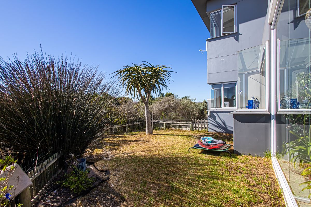 A rear garden area featuring a lawn, established tree, and timber fencing, adjacent to the side of the house with glass-enclosed patio space.