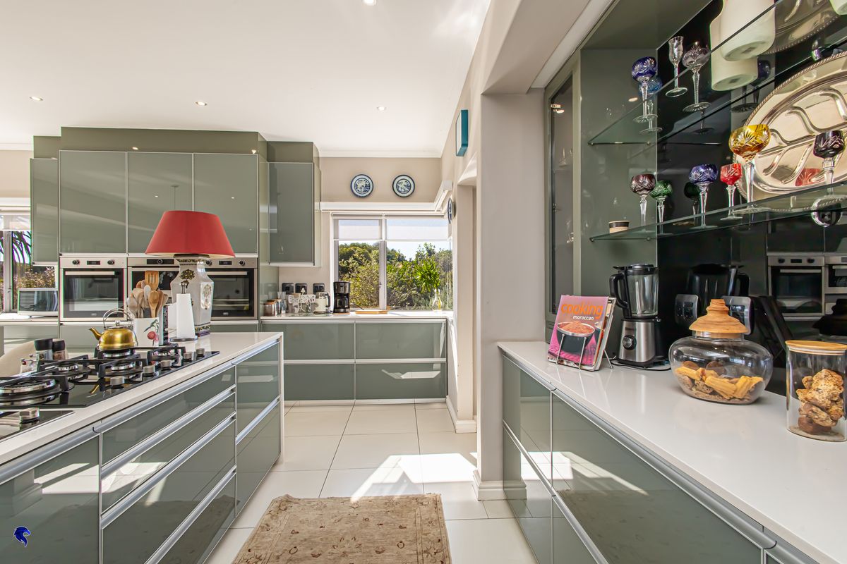 Modern kitchen featuring high-gloss cabinetry, a central island with a built-in gas hob, integrated ovens, and sleek stone countertops.