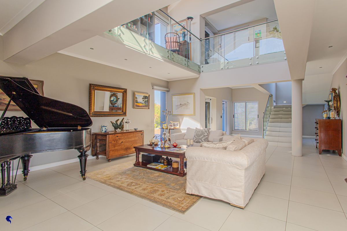 Spacious double-volume living area featuring a mezzanine level, glass balustrades, tiled flooring, and an open-plan design with a staircase.