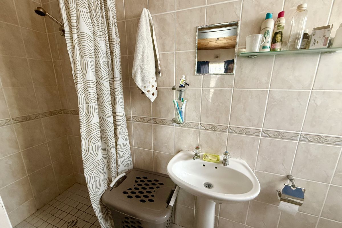 A functional bathroom featuring a pedestal sink, shower area with tiled walls, and a wall-mounted mirror.