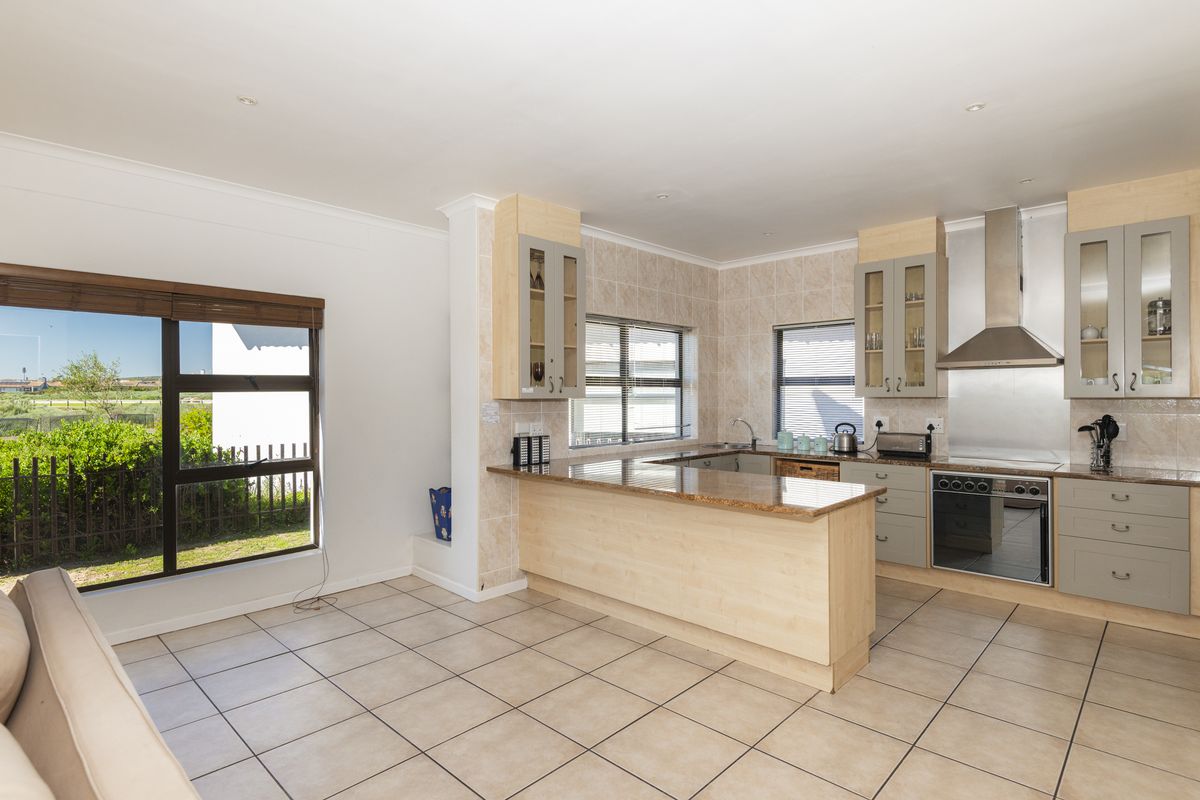 A functional kitchen featuring light wood cabinetry, granite countertops, a built-in oven, and a stainless steel extractor fan, with tiled flooring throughout.
