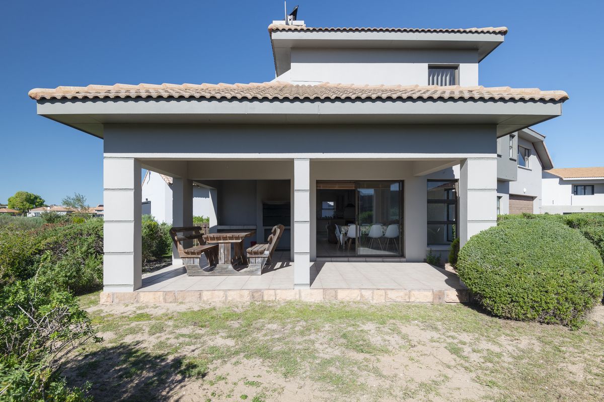 Rear view of the house featuring a covered patio with a built-in braai, tiled flooring, and sliding door access to the interior living space.
