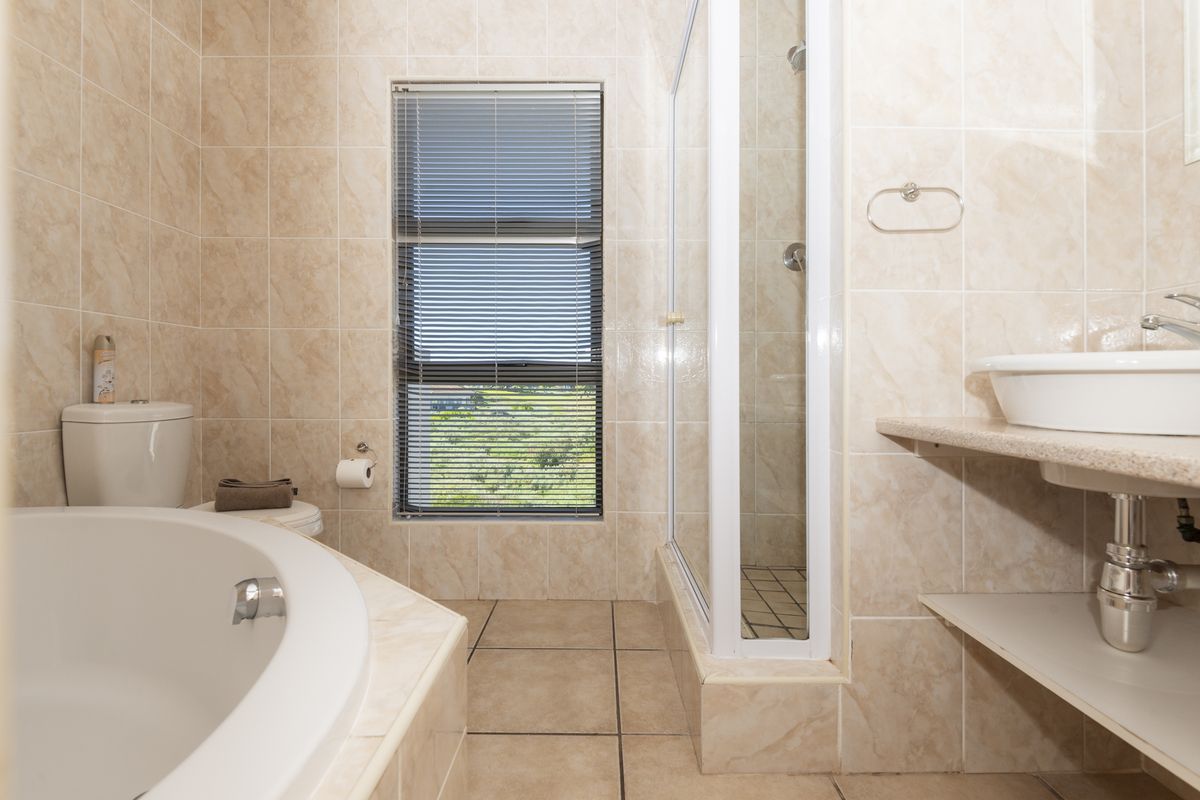 A functional bathroom featuring a built-in bathtub, separate shower enclosure, vessel sink on a floating shelf, and neutral floor-to-ceiling wall tiles.