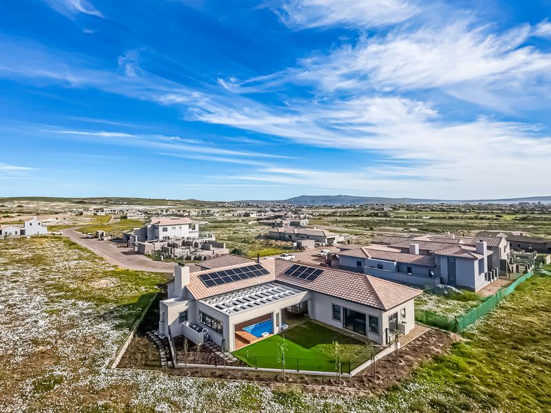 Aerial view of a modern residential property featuring solar panels, a private swimming pool, and a landscaped garden in a coastal estate setting.