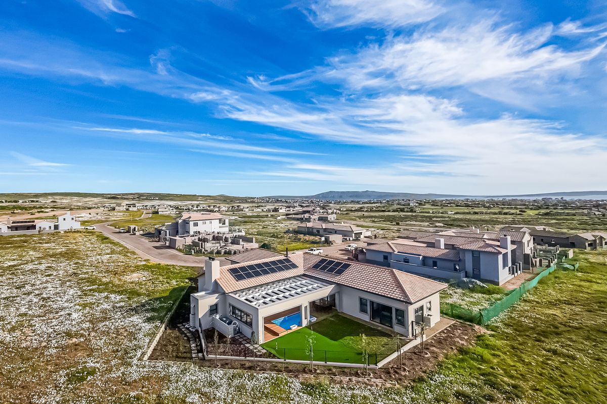 Aerial view of a modern residential property featuring solar panels, a private swimming pool, and a landscaped garden in a coastal estate setting.