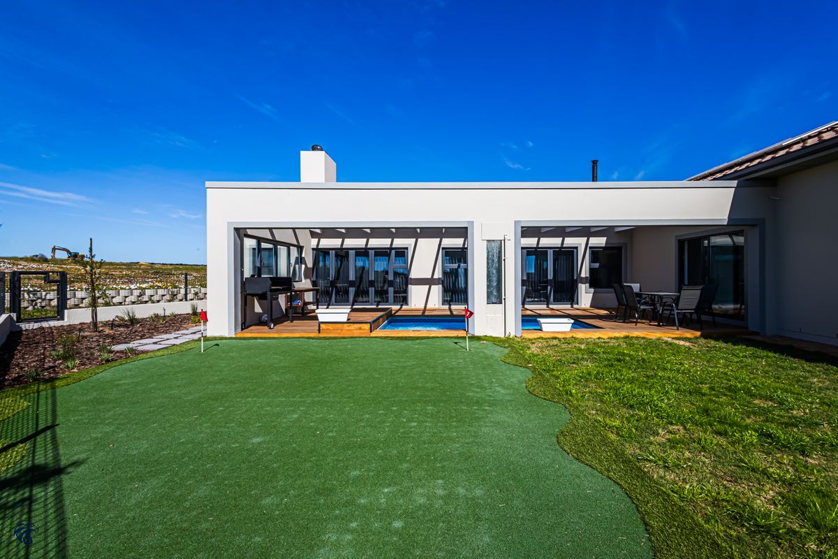 Rear exterior view featuring a covered patio with wooden decking, a swimming pool, and a private artificial grass putting green.