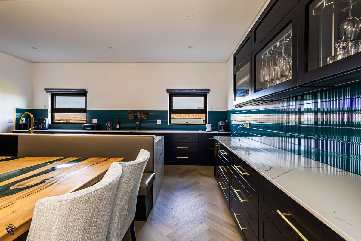 Modern kitchen featuring dark cabinetry, marble countertops, a striking teal tiled backsplash, and herringbone wood flooring with integrated dining seating.