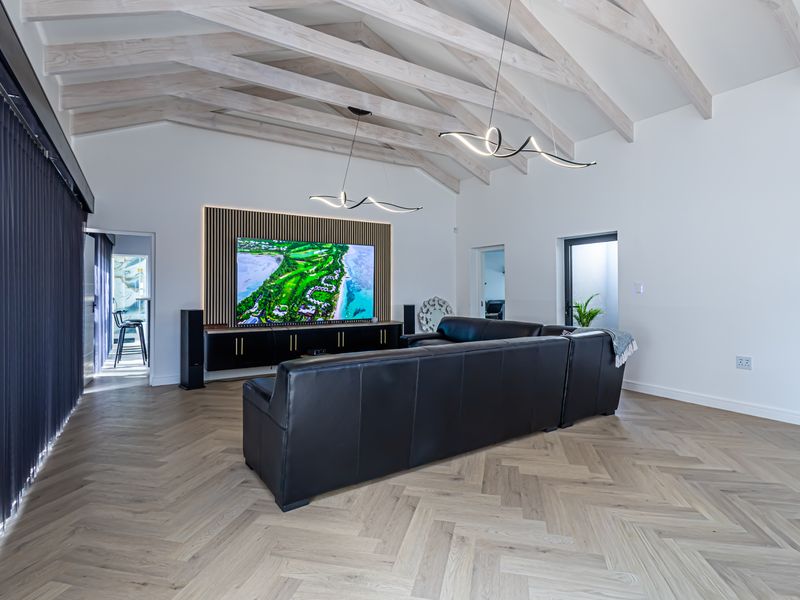 Spacious living room featuring a vaulted ceiling with exposed timber beams, herringbone flooring, and a custom built-in media wall with integrated cabinetry.
