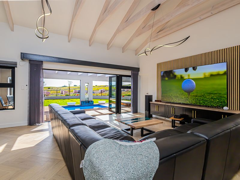 Spacious living room featuring exposed timber rafters, herringbone flooring, and seamless indoor-outdoor flow through stacking glass doors to the pool area.
