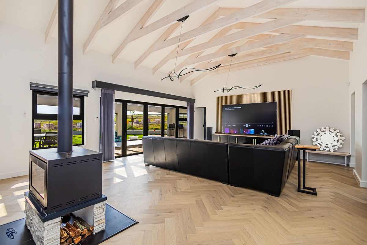 Spacious living room featuring high vaulted ceilings with exposed timber rafters, herringbone flooring, a modern freestanding fireplace, and large sliding doors leading to the patio.