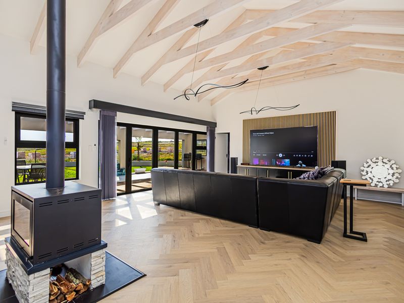 Spacious living room featuring high vaulted ceilings with exposed timber rafters, herringbone flooring, a modern freestanding fireplace, and large sliding doors leading to the patio.
