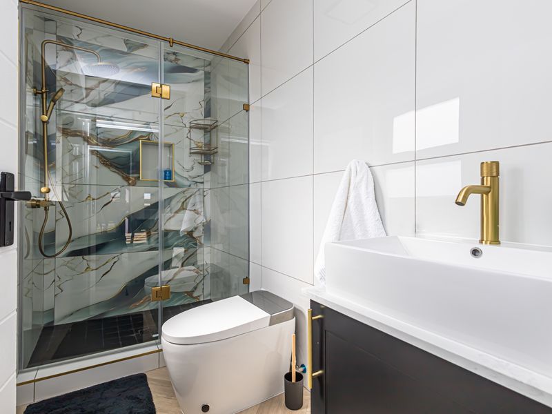 Modern bathroom featuring a walk-in shower with marble-effect tiling, brass fixtures, a vessel sink, and a sleek vanity cabinet.