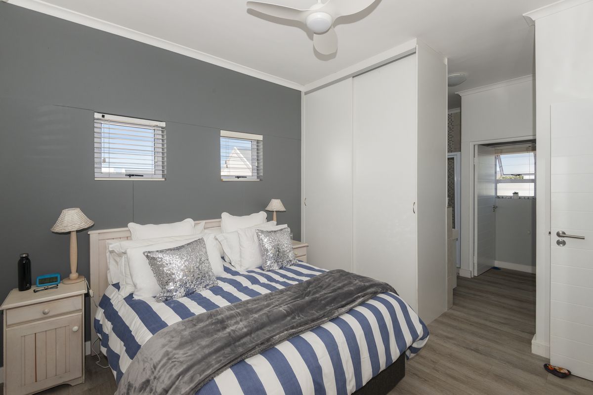 A well-maintained bedroom featuring laminate flooring, a built-in wardrobe, ceiling fan, and dual windows with venetian blinds.