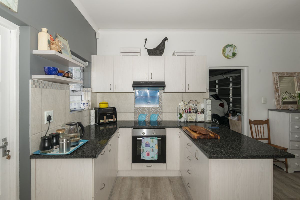 A functional kitchen featuring light-toned cabinetry, dark granite countertops, a built-in oven, and an electric hob with a tiled backsplash.