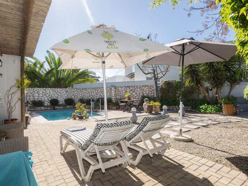A private outdoor pool area featuring a paved patio, stone boundary wall, and a covered veranda space, ideal for relaxation and outdoor entertaining.