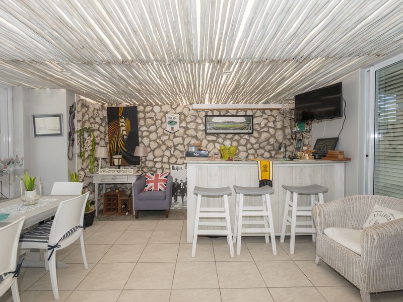 A rustic-style indoor bar area featuring a stone feature wall, unique thatched ceiling, and tiled flooring, creating a cozy entertainment space.