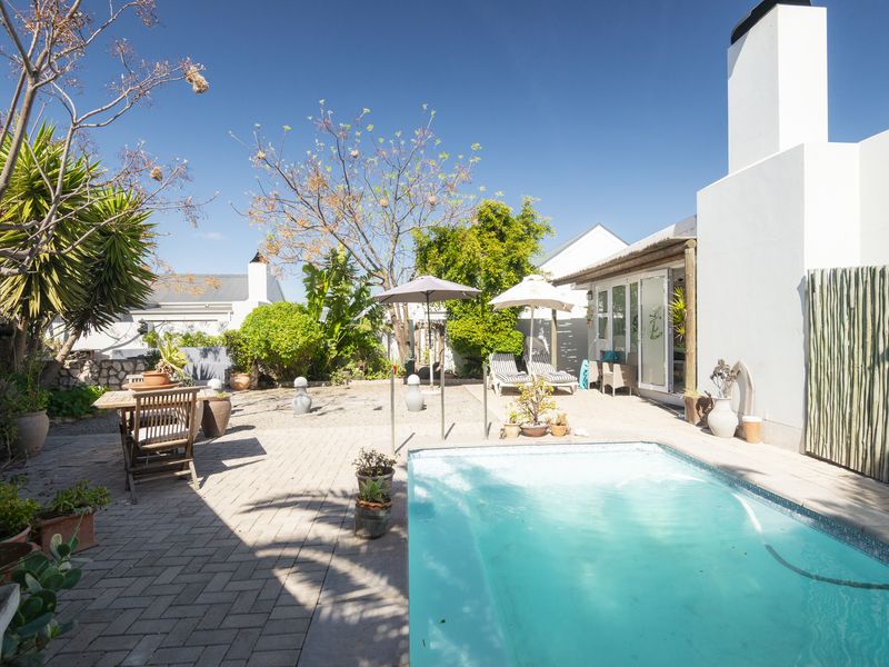 A sunny outdoor pool area featuring a paved patio, swimming pool, and direct access to the home through sliding glass doors.