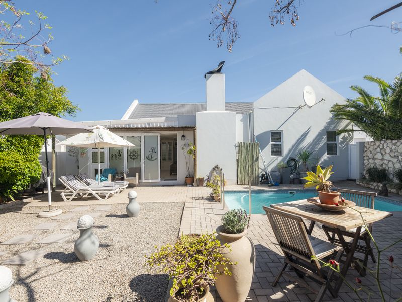 Rear exterior view featuring a swimming pool, paved patio area, gravel garden, and stone boundary wall, providing a private outdoor entertainment space.
