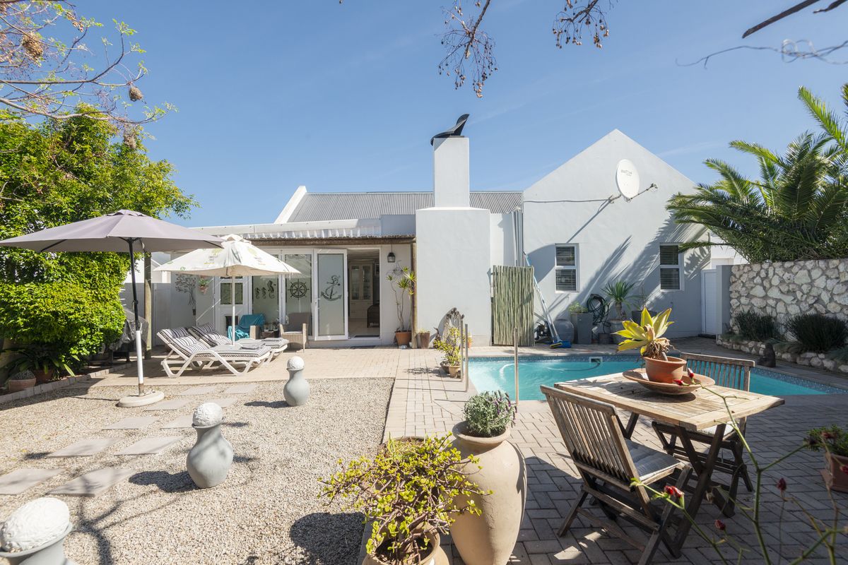 Rear exterior view featuring a swimming pool, paved patio area, gravel garden, and stone boundary wall, providing a private outdoor entertainment space.