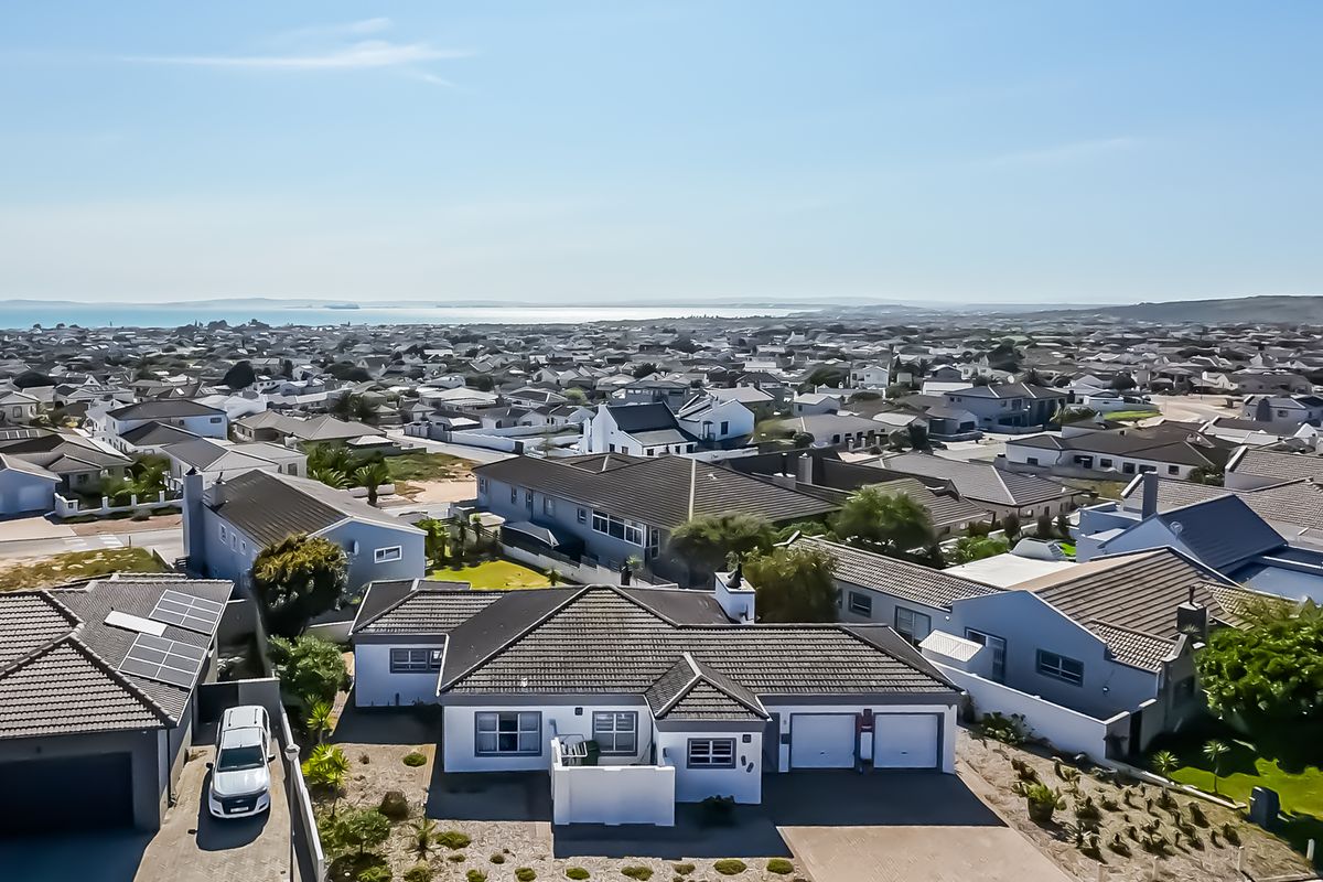 Aerial view of the residential property showing the roof structure, double garage, solar panels, and surrounding neighbourhood with distant coastal views.
