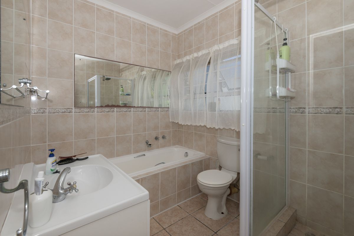 A functional bathroom featuring a built-in bathtub, separate shower enclosure, vanity basin, and neutral ceramic tiling throughout.