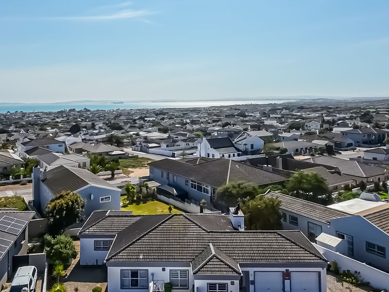 An elevated aerial view of a residential neighborhood featuring multiple homes with tiled roofs, solar panels, and surrounding coastal landscape.