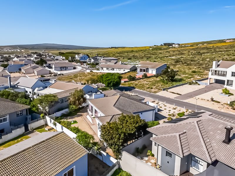 An aerial view of a residential neighborhood featuring various houses with tiled roofs, paved driveways, and landscaped surroundings under a clear blue sky.