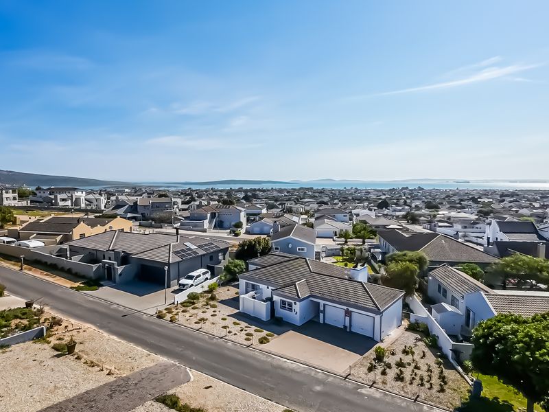 An elevated aerial view of a residential neighborhood featuring modern homes with tiled roofs, solar panels, and paved driveways under a clear blue sky.