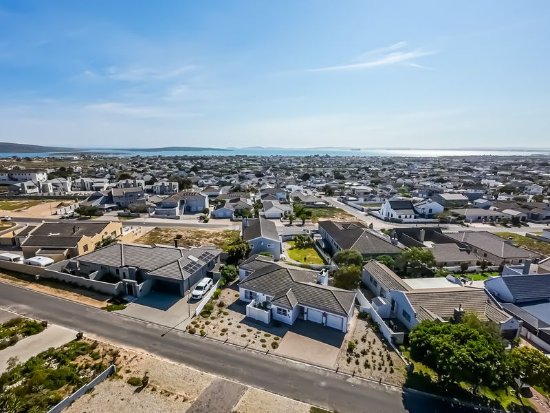 An elevated aerial view of a residential neighborhood, showcasing the surrounding street layout, housing density, and distant coastal landscape.