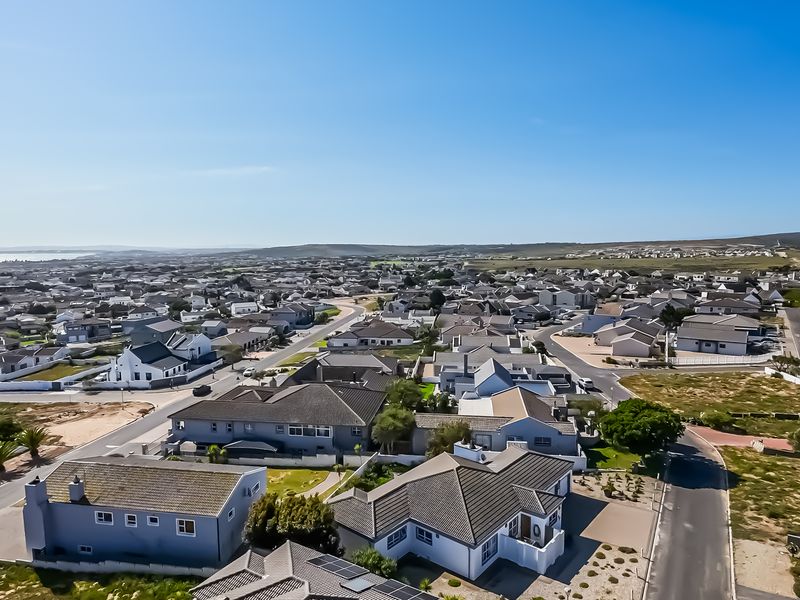 An elevated aerial view of a coastal residential estate, showcasing the surrounding neighborhood, street layout, and housing density.