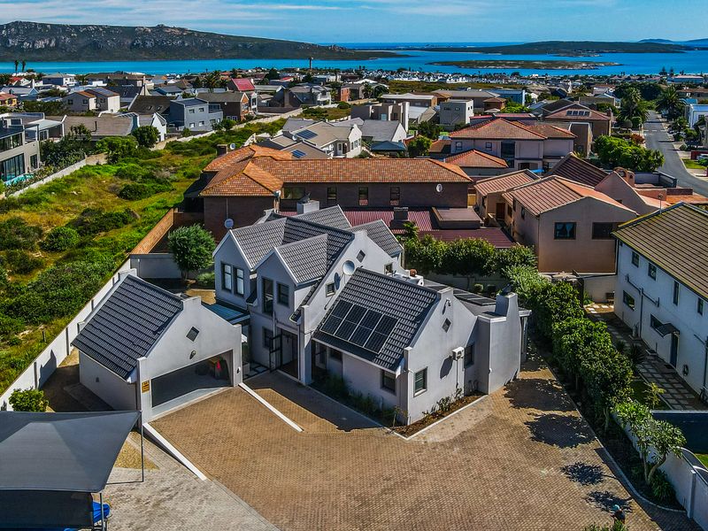 Aerial view of a modern residential property featuring a tiled roof with solar panels, a paved driveway, and a double garage in a coastal neighborhood.