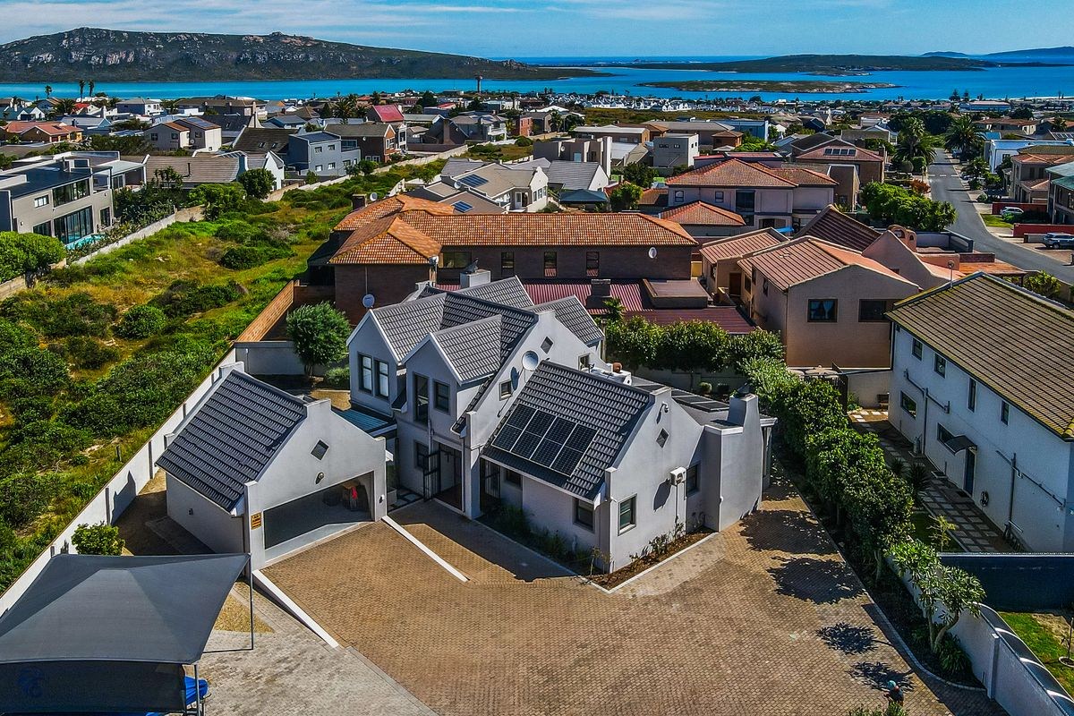Aerial view of a modern residential property featuring a tiled roof with solar panels, a paved driveway, and a double garage in a coastal neighborhood.