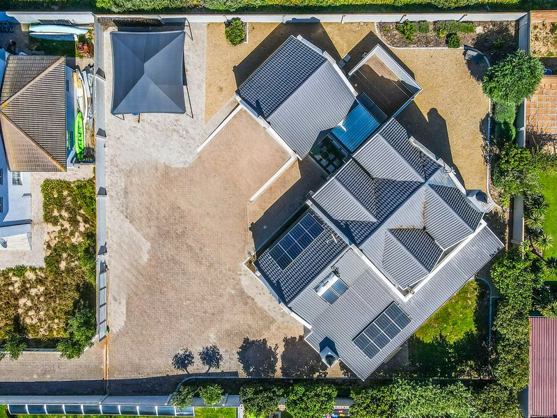 Aerial view of the property showcasing the roof structure, solar energy installations, paved driveway, and surrounding garden area.