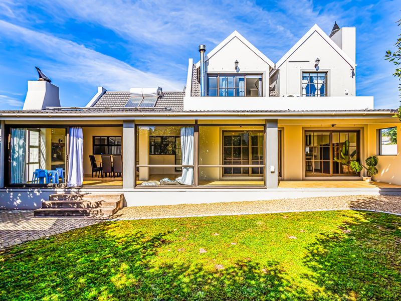 Rear view of a two-story house featuring a covered patio, large sliding glass doors, a tiled roof with solar panels, and a landscaped garden.