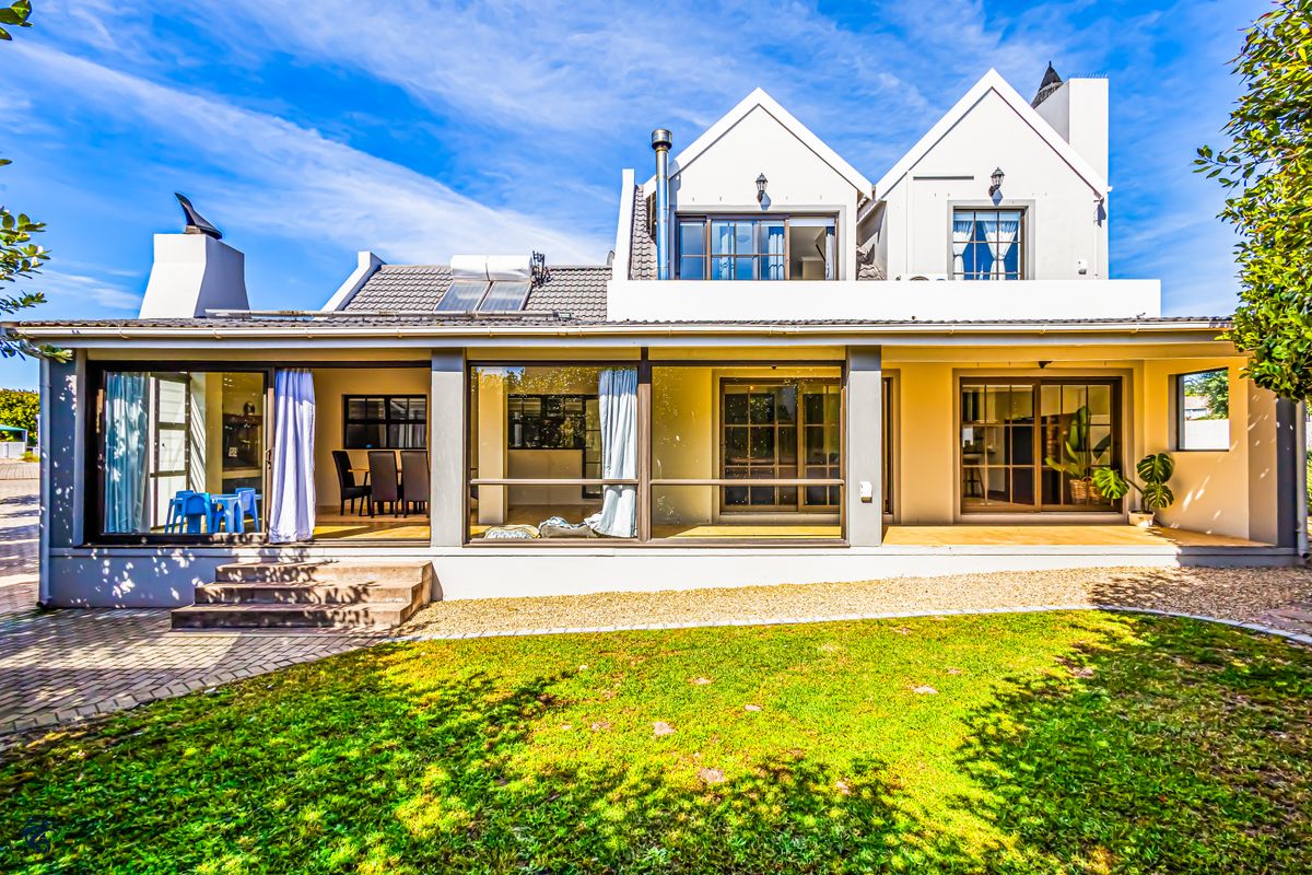 Rear view of a two-story house featuring a covered patio, large sliding glass doors, a tiled roof with solar panels, and a landscaped garden.