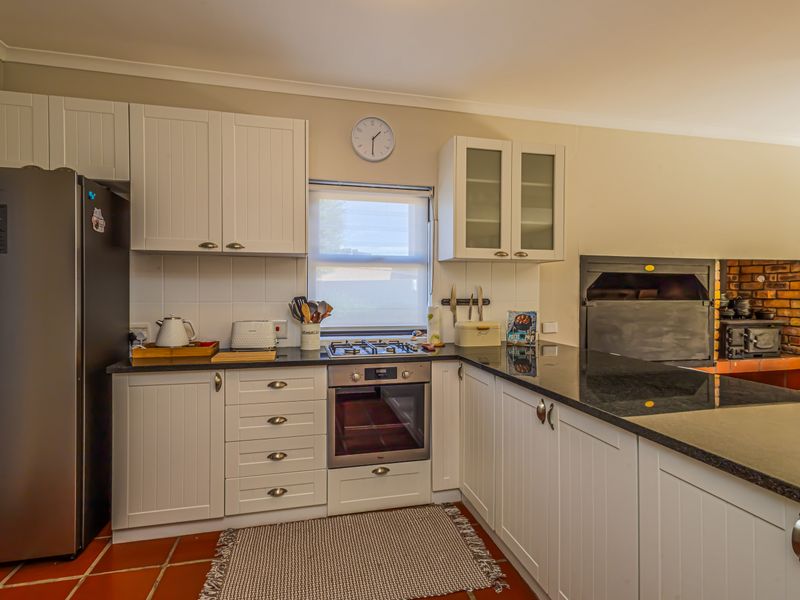 A well-maintained kitchen featuring white cabinetry, granite countertops, a gas hob, built-in oven, and a traditional indoor braai area with terracotta flooring.