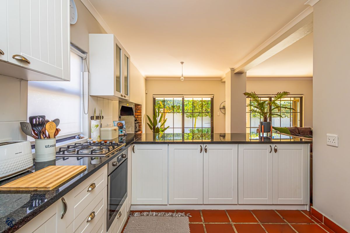 A well-maintained kitchen featuring white cabinetry, granite countertops, a gas hob, and built-in oven, with terracotta flooring and direct access to the outdoor area.