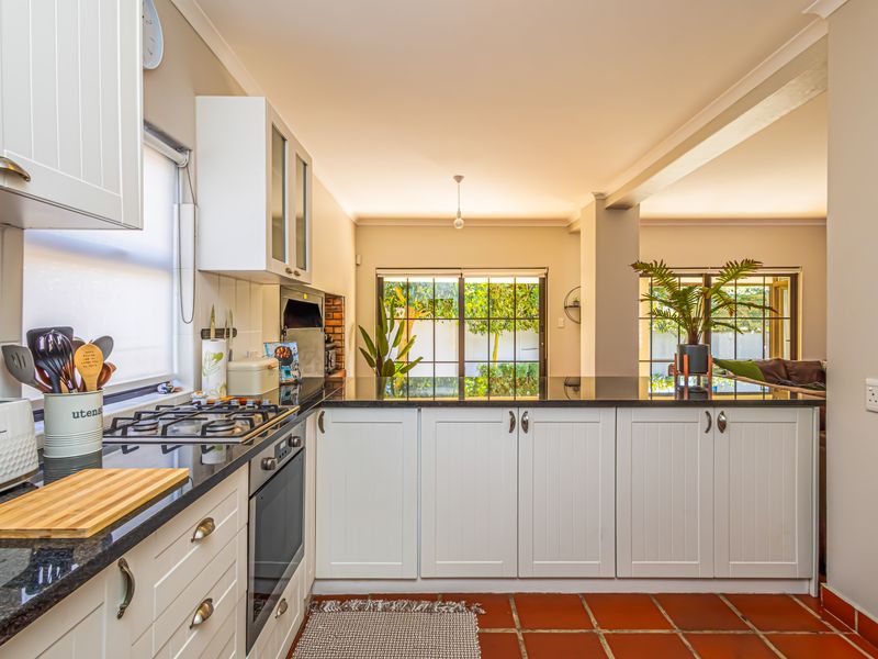 A well-maintained kitchen featuring white cabinetry, granite countertops, a gas hob, and built-in oven, with terracotta flooring and direct access to the outdoor area.