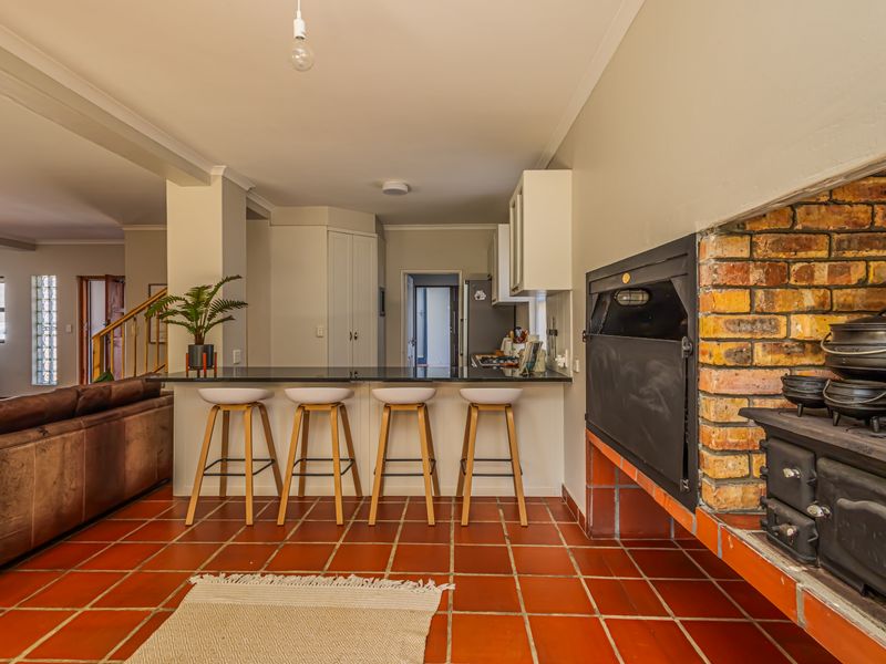 Open-plan living area featuring a built-in brick fireplace, terracotta tiled flooring, and a breakfast bar with granite countertops connecting to the kitchen.