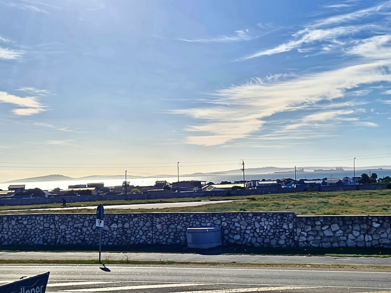 A scenic view overlooking a vacant residential plot with a stone boundary wall and distant coastal landscape.