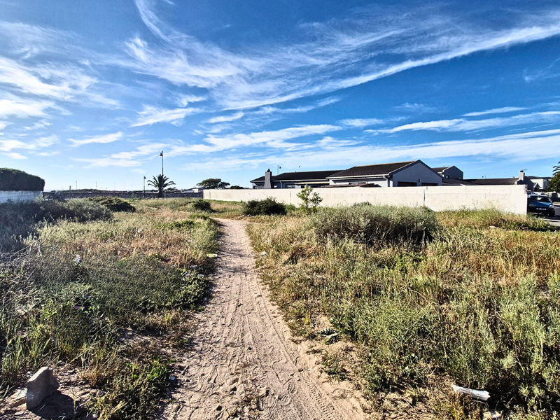 A vacant residential plot featuring a dirt path and perimeter walling, situated in a developed neighborhood setting.