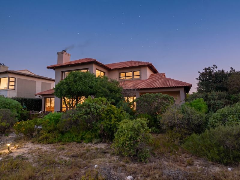 A beautiful twilight view of the rear elevation of a two-story house featuring a terracotta tile roof, chimney, and established garden.