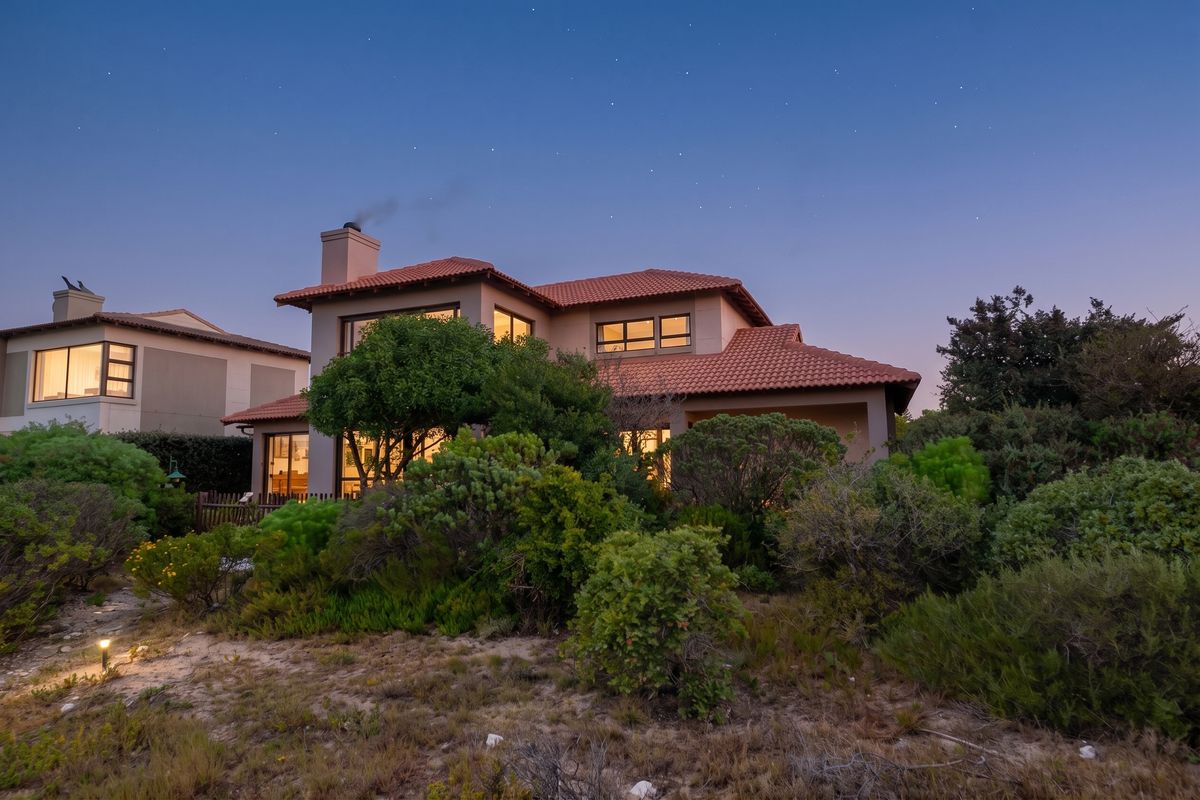 A beautiful twilight view of the rear elevation of a two-story house featuring a terracotta tile roof, chimney, and established garden.