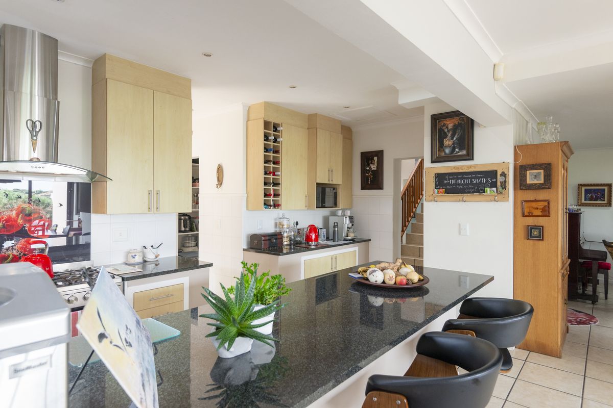 A functional kitchen featuring granite countertops, light wood cabinetry, a gas hob with stainless steel extractor, and a breakfast bar island.