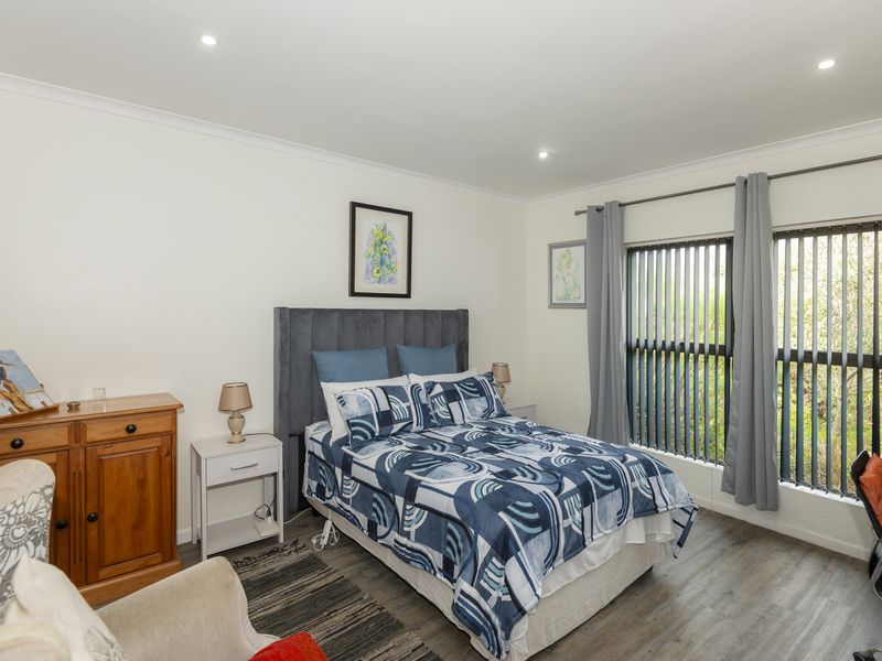 A well-maintained bedroom featuring laminate flooring, recessed downlighting, and large windows with vertical blinds, offering a bright and functional living space.